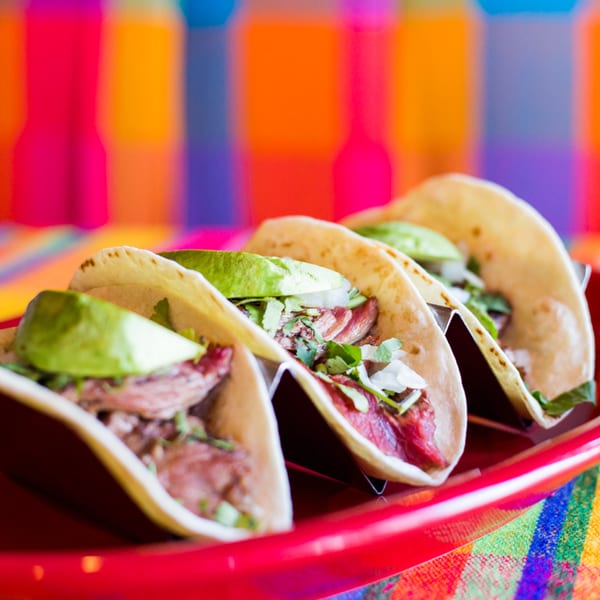 Three El Don Mexican Restaurant tacos with meat, cilantro, onions, and avocado slices on a red tray.