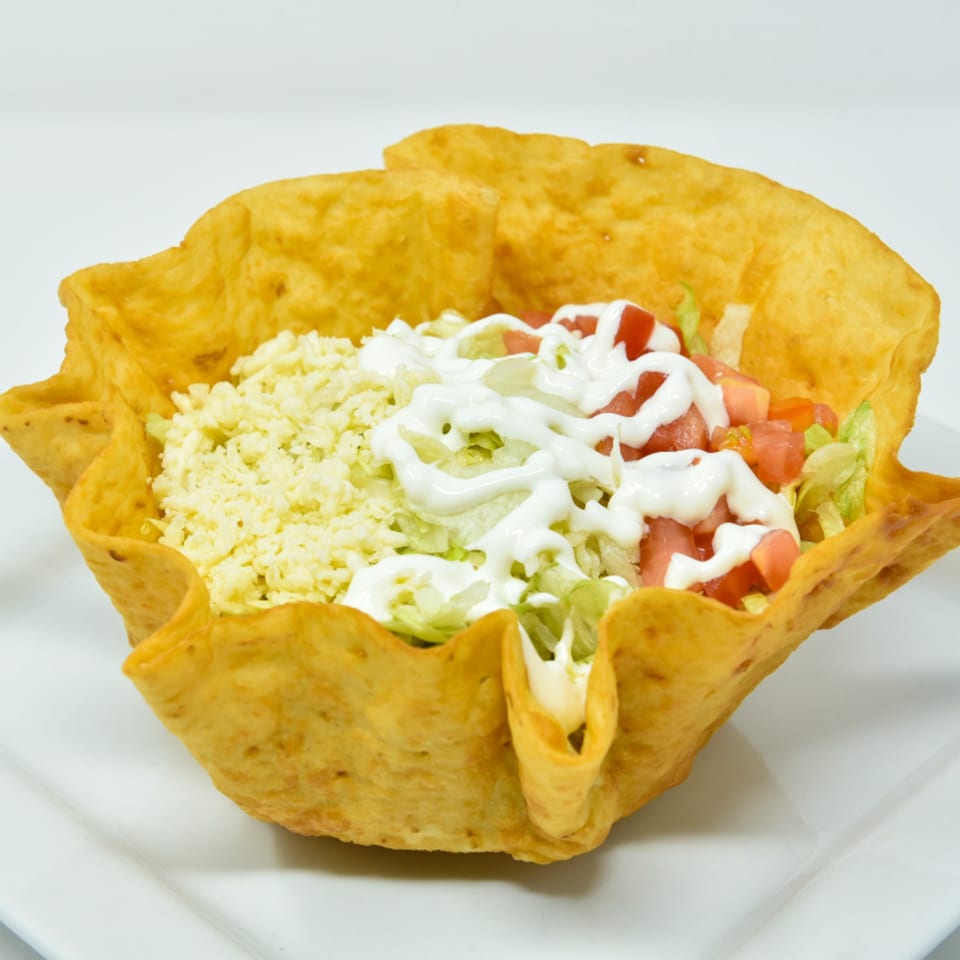 A taco salad in a crispy fried tortilla bowl, topped with cheese, lettuce, tomatoes, and sour cream.