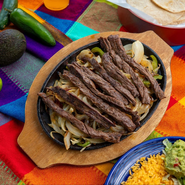 Sizzling beef fajitas with onions and peppers, served with rice, guacamole, and tortillas.