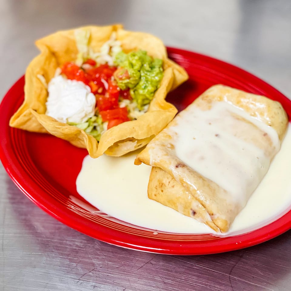 A Mexican burrito covered in white cheese sauce, next to a taco salad in a crispy shell.