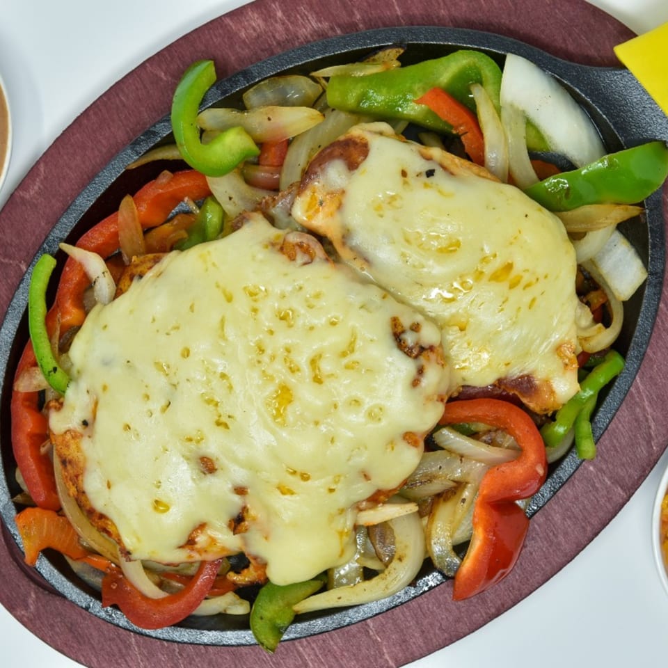 Sizzling Mexican fajitas with chicken, melted cheese, bell peppers, and onions on a dark platter.